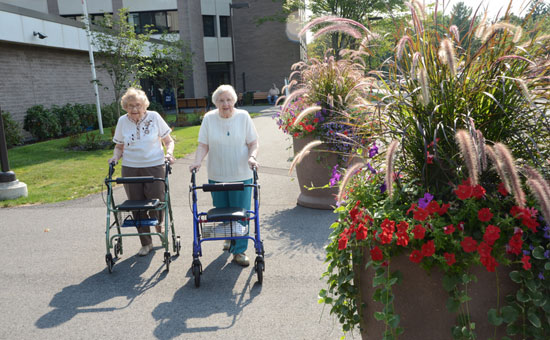 Two elderly residences walking outside with walkers
