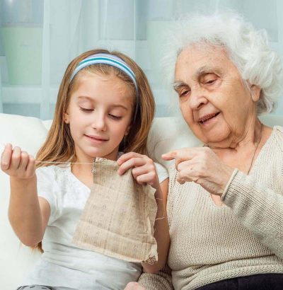 senior woman teaching granddaughter how to sew