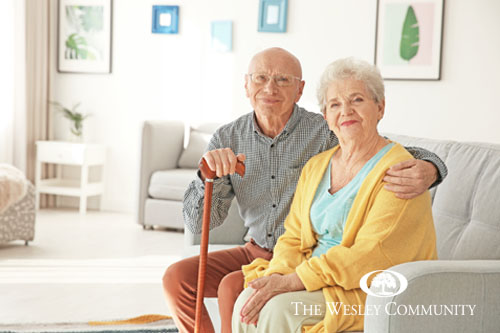 Senior couple sitting on a couch smiling at the camera.