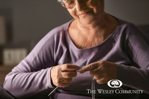 A senior woman sitting and concentrating on knitting an item.