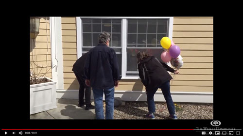 Three people with birthday balloons looking in a window