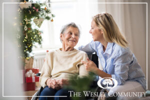 A senior woman and her daughter sitting by a christmas tree.