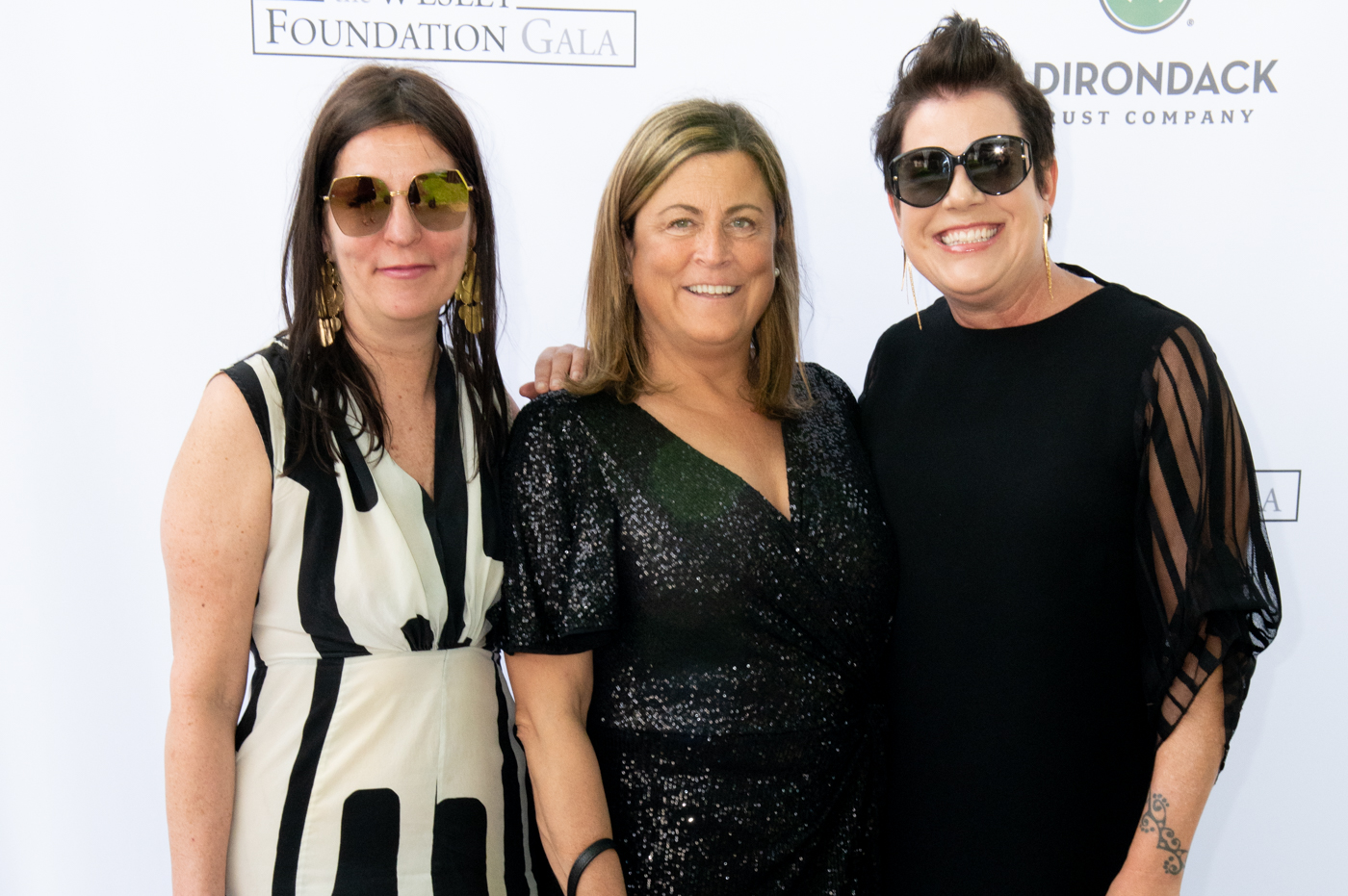 A set of three women, from left to right wearing a black and white dress, a sparkling black dress, and a black dress.