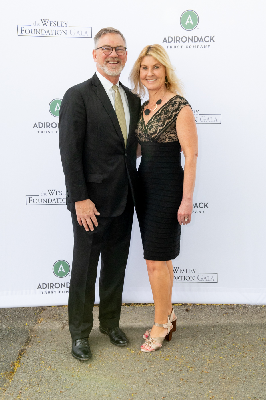 A couple posing for a picture, a man on the left wearing a black suit and a woman on the right wearing a black dress