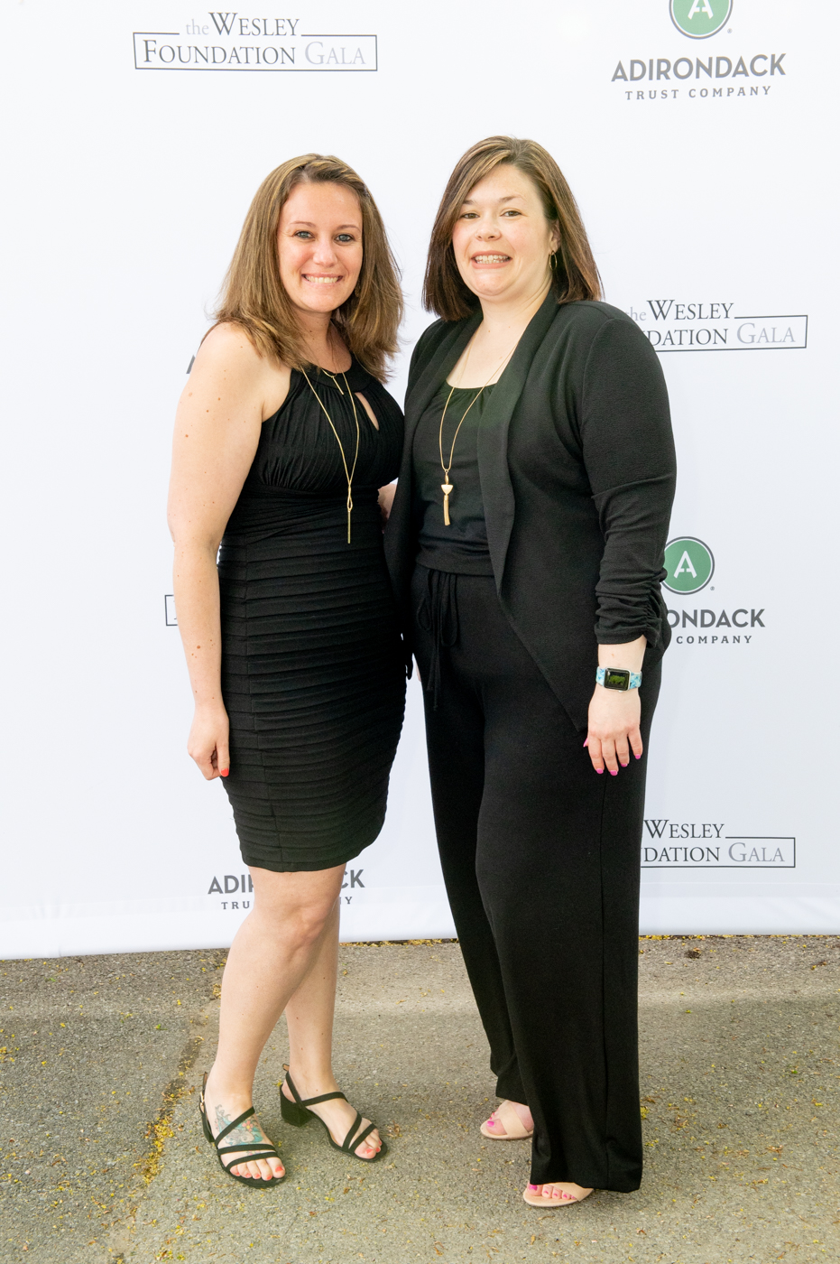 A couple posing for a picture, a woman on the left wearing a black dress and a woman on the right wearing a black dress