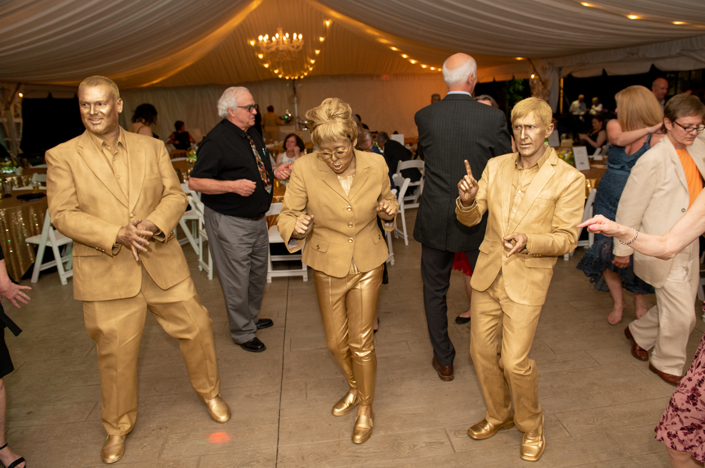3 people dress in all gold covered in gold paint dancing in large tent